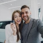 Młoda para robi selfie przy świeżo kupionym samochodzie w salonie