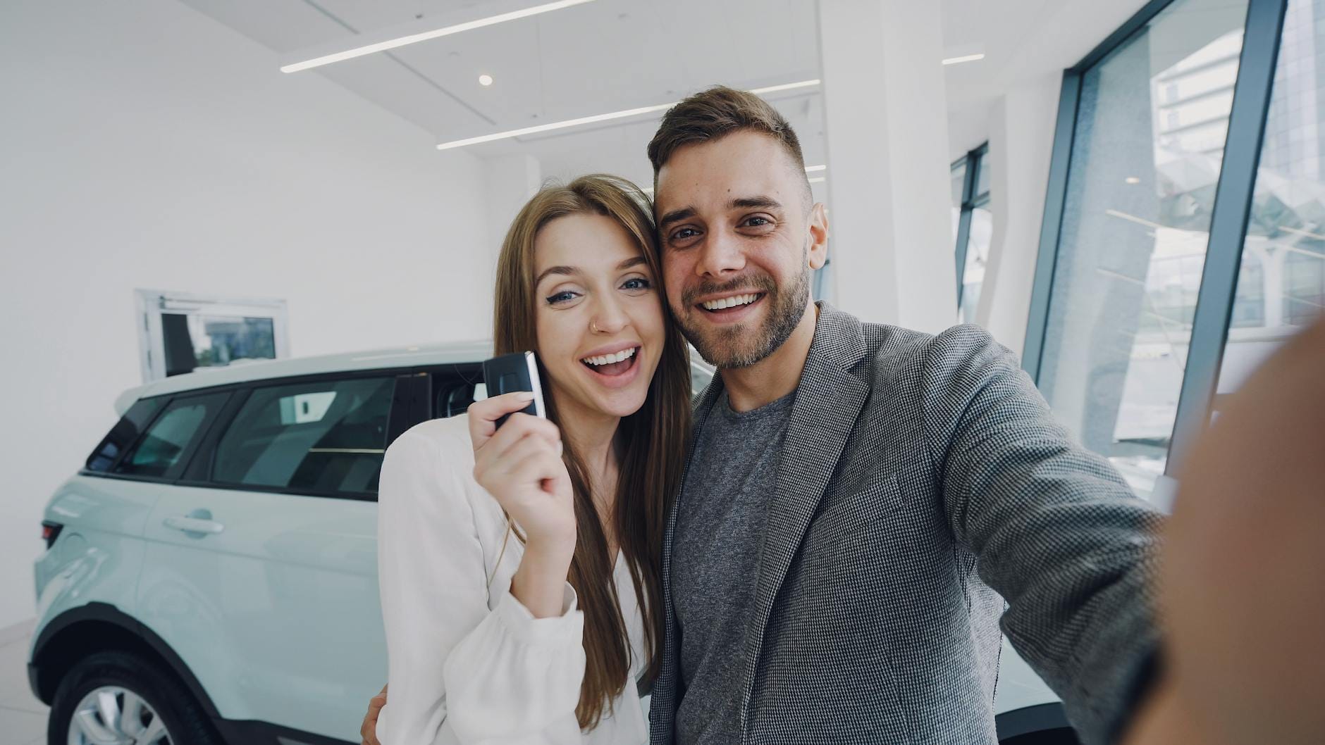 Młoda para robi selfie przy świeżo kupionym samochodzie w salonie