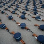 Mundurki wojskowe i karabiny ułożone w równym rzędzie na placu apelu