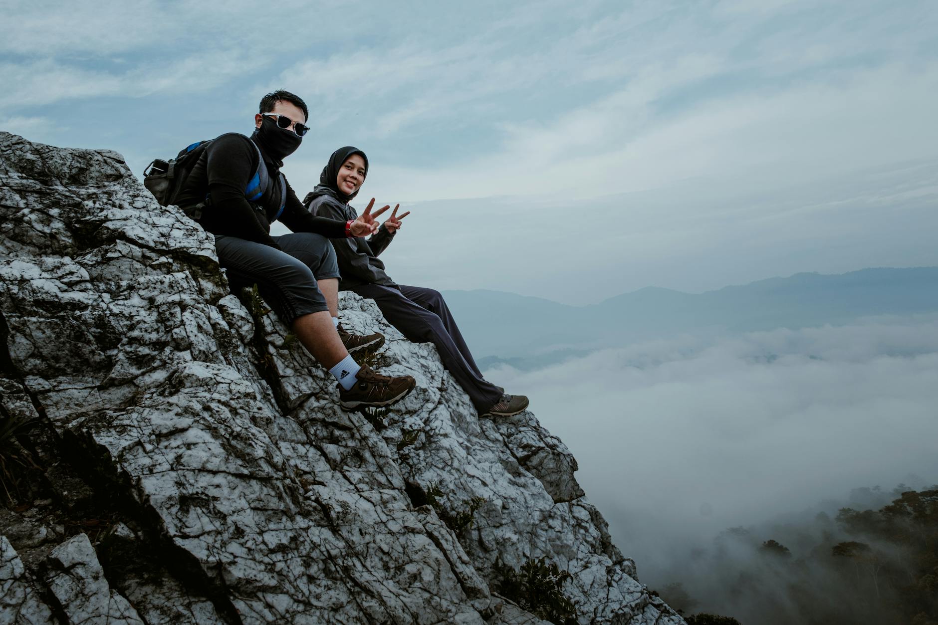 Dwóch turystów z plecakami odpoczywa na skalnym klifie ponad chmurami