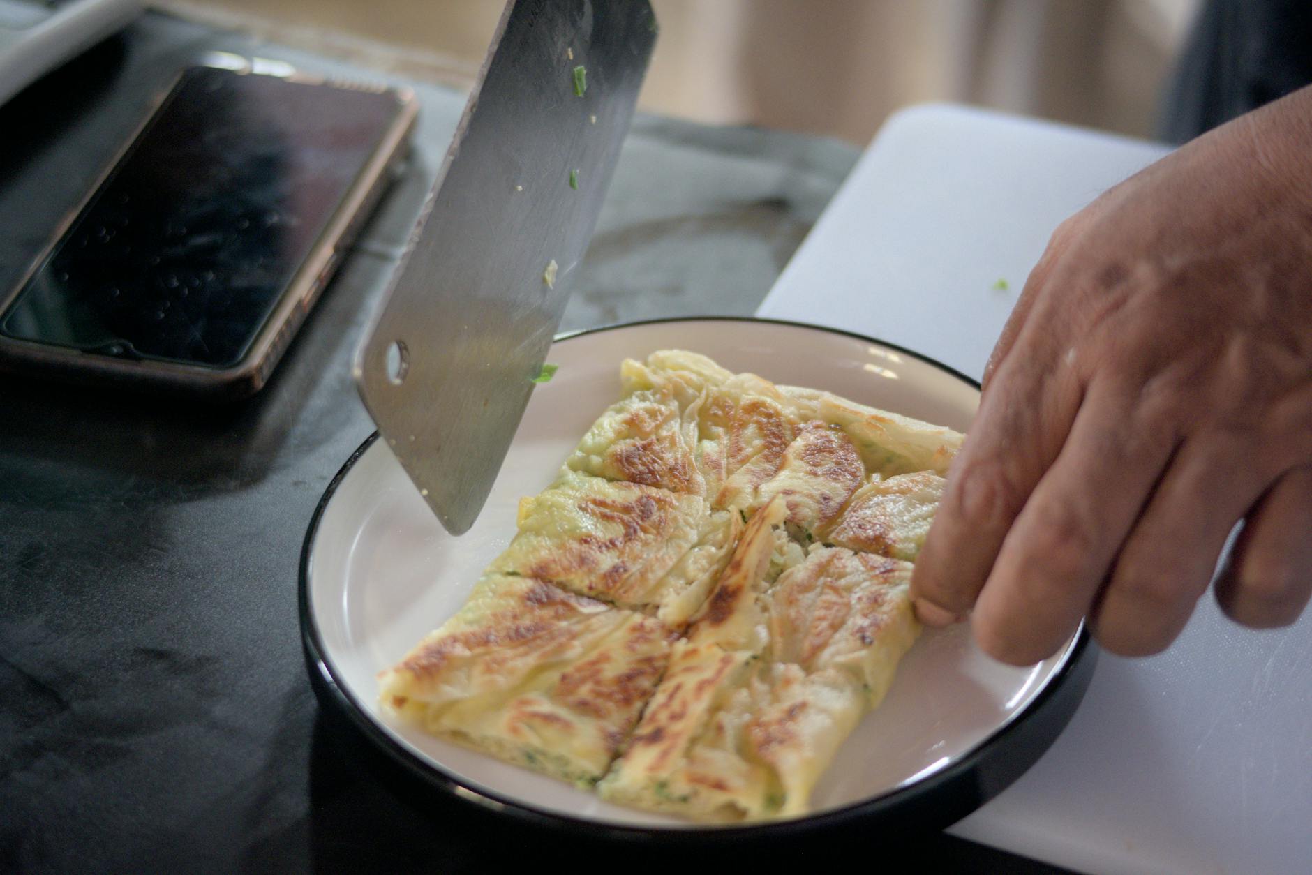 Malezyjski kucharz kroi świeżo usmażony roti canai na talerzu