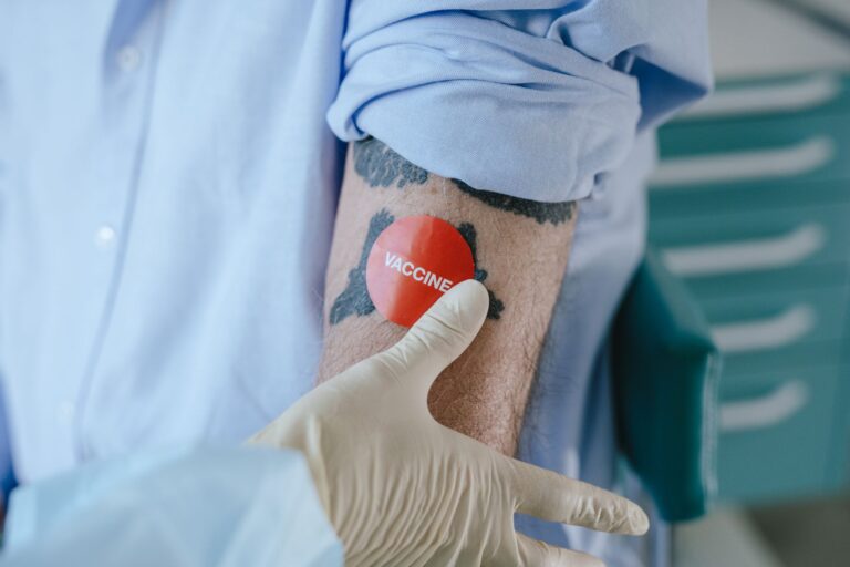 Personel medyczny nakleja plaster po szczepieniu na wytatuowanym ramieniu